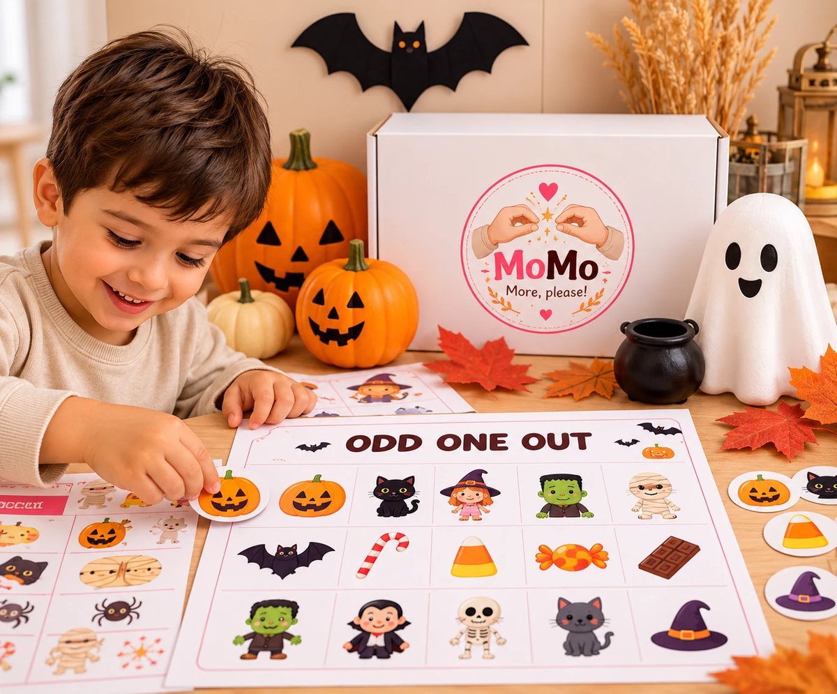 A smiling boy placing a pumpkin sticker on the Odd One Out worksheet next to the Halloween Box